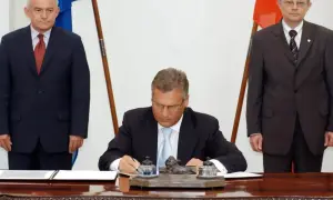 Uroczyste podpisanie dokumentów, symboliczny moment, kiedy Polska weszła do Unii. Trzech mężczyzn w garniturach, flagi Polski i UE.