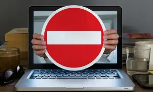 Ręce trzymają znak zakazu przed ekranem laptopa. Symbolizuje to debatę o konfederacji a wolności słowa, projekt ustawy o ochronie w internecie.