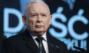 Jarosław Kaczyński w garniturze, na tle niebieskiego napisu.