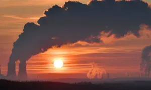 Zachód słońca nad przemysłowym krajobrazem, gdzie dymiące kominy kontrastują z pomarańczowym niebem. To obraz, który może symbolizować wyzwania związane z polityką klimatyczną i stosunkiem PiS do Zielonego Ładu.