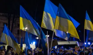Zwolennicy pomocy militarnej dla Ukrainy i polityki obronnej kraju, z ukraińskimi flagami na nocnym wiecu.