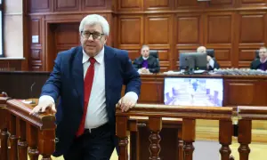 Mężczyzna w garniturze i krawacie wchodzi na salę sądową. Sędziowie w togach siedzą za stołem. Proces polityków PiS trwa.