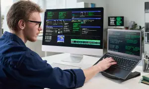 Programista pracuje przy wielu monitorach. Dowiedz się, co Konfederacja proponuje dla branży IT i programistów B2B.