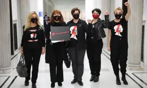 Kobiety w czarnych koszulkach "Strajk Kobiet" i maskach, z hasłem "Wyrok na kobiety", symbolizują siłę lewicy i jej zaangażowanie w protesty.