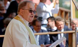 Ojciec Tadeusz Rydzyk przemawia do mikrofonu. W tle widać ludzi, a także fragmenty budowli. W czasach rządu PiS, fundacje związane z ojcem Rydzykiem otrzymywały znaczące dotacje.