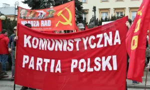 Ludzie niosą czerwony transparent "KOMUNISTYCZNA PARTIA POLSKI" i flagę z sierpem i młotem. To manifestacja poparcia dla socjalizmu.