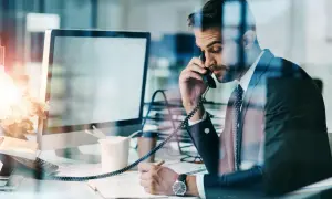 Biznesmen w garniturze rozmawia przez telefon, notując. Czasem nawet siła wyższa nie przeszkodzi w pracy.