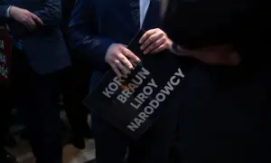 Mężczyzna w garniturze trzyma czarną tabliczkę z napisami: KORWIN, BRAUN, LIROY, NARODOWCY. To może być odpowiedź na pytanie, dlaczego młodzi mężczyźni głosują na Konfederację zamiast na lewicę.