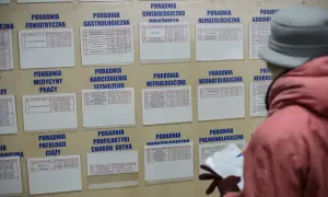 Pacjentka analizuje tablicę z grafikami poradni, szukając informacji o tym, jak koalicja obywatelska chce zmienić system ochrony zdrowia.