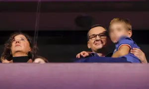 Mateusz Morawiecki z dziećmi, uśmiechnięty, trzyma na rękach jedno z dzieci. Obok kobieta patrzy w górę.