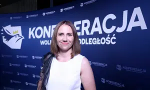 Uśmiechnięta kobieta na tle niebieskiego banera z logo i napisem "KONFEDERACJA WOLNOŚĆ I NIEPODLEGŁOŚĆ".