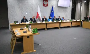 Osiem osób siedzi przy stole w sali konferencyjnej, przed nimi flagi Polski i UE.