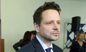 Rafał Trzaskowski, którego wykształcenie budzi zainteresowanie, w garniturze i krawacie. W tle inne osoby i tablica.