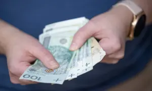 Dłonie trzymające banknoty 100 zł. Czy to już czas na rozliczenie podatku od wygranej?