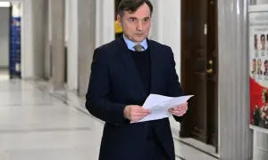 Mężczyzna w garniturze trzyma dokumenty, być może związane z aferą z Funduszem Sprawiedliwości u Ziobry i PiS.