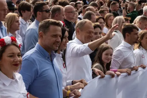 Uśmiechnięty Donald Tusk i tłum ludzi z biało-czerwonymi akcentami, wspierający platformę obywatelską.
