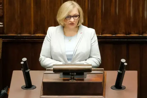 Kobieta w jasnej marynarce przemawia w sejmie, dyskutując o wpływie polityki PiS na prawa kobiet w Polsce.