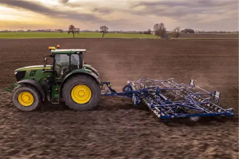 Zielony traktor z agregatem uprawowym na polu. Europejski zielony ład: dlaczego lewica popiera unijną politykę klimatyczną.