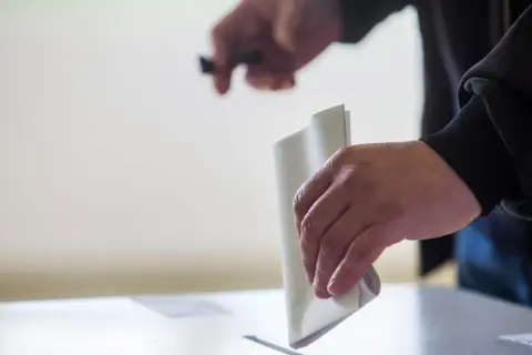 Ręka wrzuca kartę do głosowania do urny. To ważny moment, pokazujący, jak głosować.