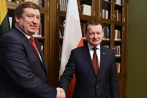Dwóch polityków ściska sobie dłonie na tle flag Polski i Litwy.