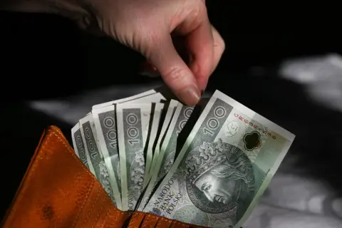 Dłoń wyciąga banknot 100 zł z brązowego portfela. Czy trzynasta i czternasta emerytura to pomysł PiS?