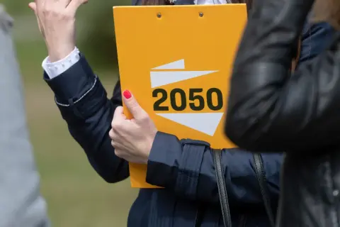 Kobieta prezentuje żółtą teczkę z napisem "2050", symbolizującą strategię polską 2050 na wybory samorządowe i europejskie.