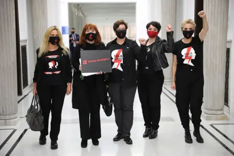 Kobiety w czarnych koszulkach "Strajk Kobiet" i maskach, z hasłem "Wyrok na kobiety", symbolizują siłę lewicy i jej zaangażowanie w protesty.