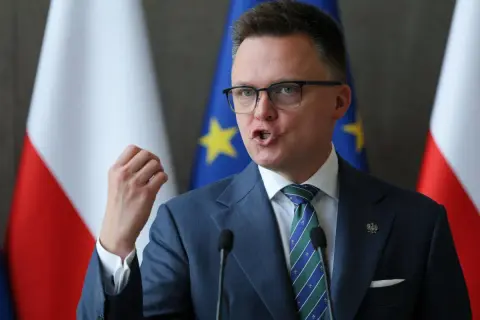Szymon Hołownia, w garniturze i z flagami Polski i UE, przemawia. Czy jest konserwatystą? Ewolucja poglądów politycznych.
