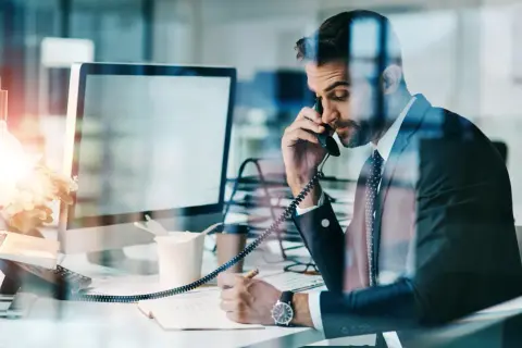 Biznesmen w garniturze rozmawia przez telefon, notując. Czasem nawet siła wyższa nie przeszkodzi w pracy.