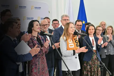 Kobieta w pomarańczowej chuście z napisem "Polska 50" przemawia. Czy Polska 2050 chce zlikwidować 800 plus?