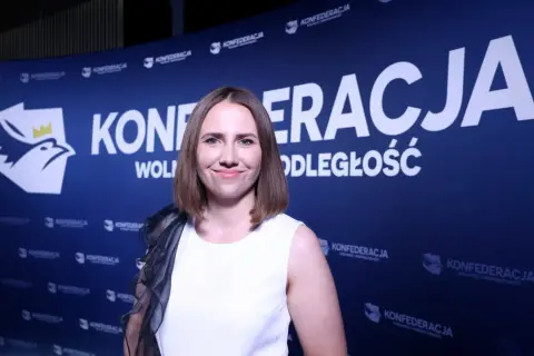Uśmiechnięta kobieta na tle niebieskiego banera z logo i napisem "KONFEDERACJA WOLNOŚĆ I NIEPODLEGŁOŚĆ".