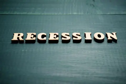 Drewniane litery układają słowo "RECESSION". To pojęcie ekonomiczne, które opisuje spowolnienie gospodarcze.