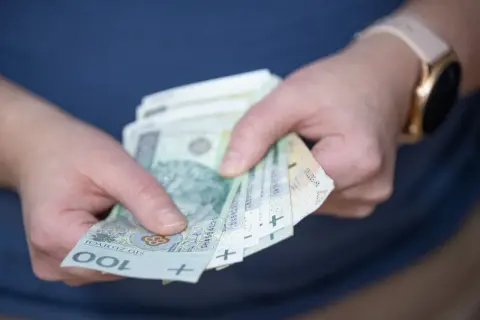 Dłonie trzymające banknoty 100 zł. Czy to już czas na rozliczenie podatku od wygranej?