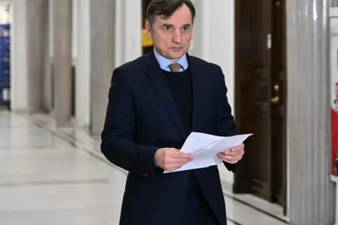 Mężczyzna w garniturze trzyma dokumenty, być może związane z aferą z Funduszem Sprawiedliwości u Ziobry i PiS.