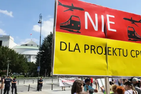 Protestujący sprzeciwiają się projektowi CPK. Transparent "NIE DLA PROJEKTU CPK" z symbolami samolotu i pociągu.