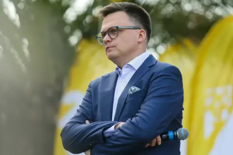 Mężczyzna w garniturze, z okularami, z mikrofonem w dłoni. Symboliczne przedstawienie debaty: Polska 2050 vs Nowa Lewica, główne osie sporu ideologicznego.
