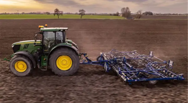 Zielony traktor z agregatem uprawowym na polu. Europejski zielony ład: dlaczego lewica popiera unijną politykę klimatyczną.