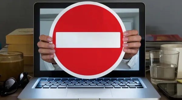 Ręce trzymają znak zakazu przed ekranem laptopa. Symbolizuje to debatę o konfederacji a wolności słowa, projekt ustawy o ochronie w internecie.
