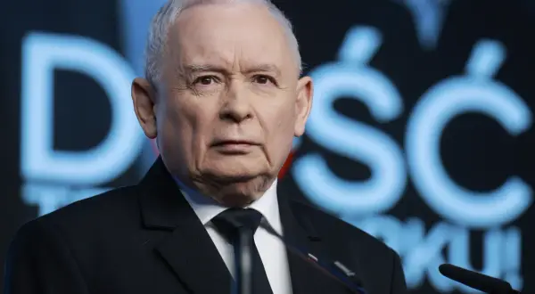 Jarosław Kaczyński w garniturze, na tle niebieskiego napisu.