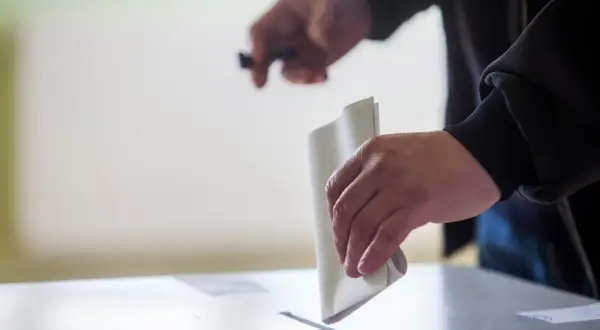 Ręka wrzuca kartę do głosowania do urny. To ważny moment, pokazujący, jak głosować.
