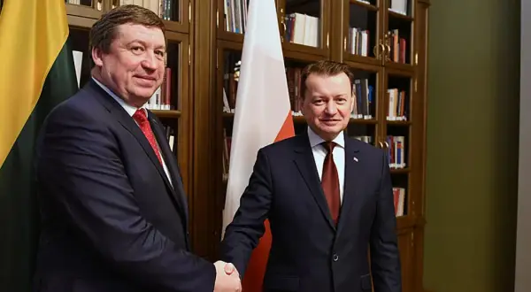 Dwóch polityków ściska sobie dłonie na tle flag Polski i Litwy.