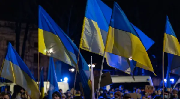 Zwolennicy pomocy militarnej dla Ukrainy i polityki obronnej kraju, z ukraińskimi flagami na nocnym wiecu.