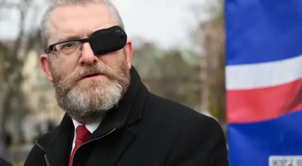 Grzegorz Braun w Sejmie, skandale i realne poparcie dla partii. Mężczyzna w okularach i opasce na oku, na tle flagi.