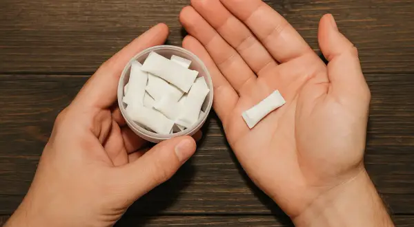 Dłonie trzymające pojemnik z białymi woreczkami nikotynowymi i jeden woreczek na dłoni. Czy snus jest legalny w Polsce?
