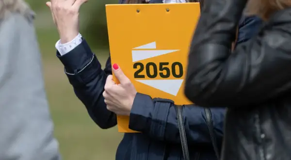 Kobieta prezentuje żółtą teczkę z napisem "2050", symbolizującą strategię polską 2050 na wybory samorządowe i europejskie.