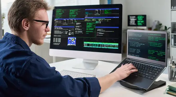 Programista pracuje przy wielu monitorach. Dowiedz się, co Konfederacja proponuje dla branży IT i programistów B2B.