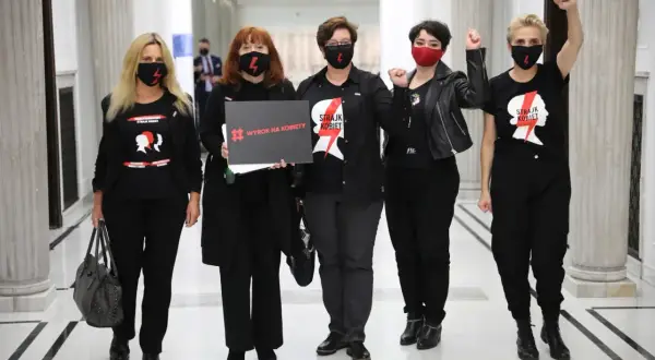 Kobiety w czarnych koszulkach "Strajk Kobiet" i maskach, z hasłem "Wyrok na kobiety", symbolizują siłę lewicy i jej zaangażowanie w protesty.