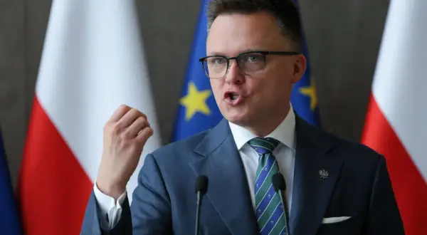 Szymon Hołownia, w garniturze i z flagami Polski i UE, przemawia. Czy jest konserwatystą? Ewolucja poglądów politycznych.