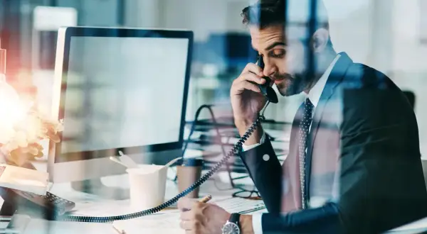 Biznesmen w garniturze rozmawia przez telefon, notując. Czasem nawet siła wyższa nie przeszkodzi w pracy.