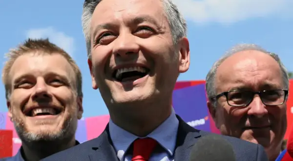 Uśmiechnięty polityk z czerwonym krawatem, w otoczeniu innych mężczyzn. Analiza struktury elektoratu partii, kogo reprezentuje lewica.